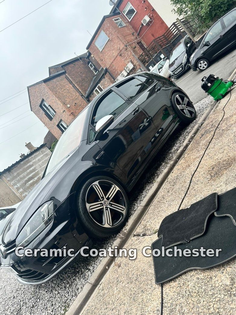 Black Volkswagen Golf being detailed at the roadside with mats removed and a wet vacuum running